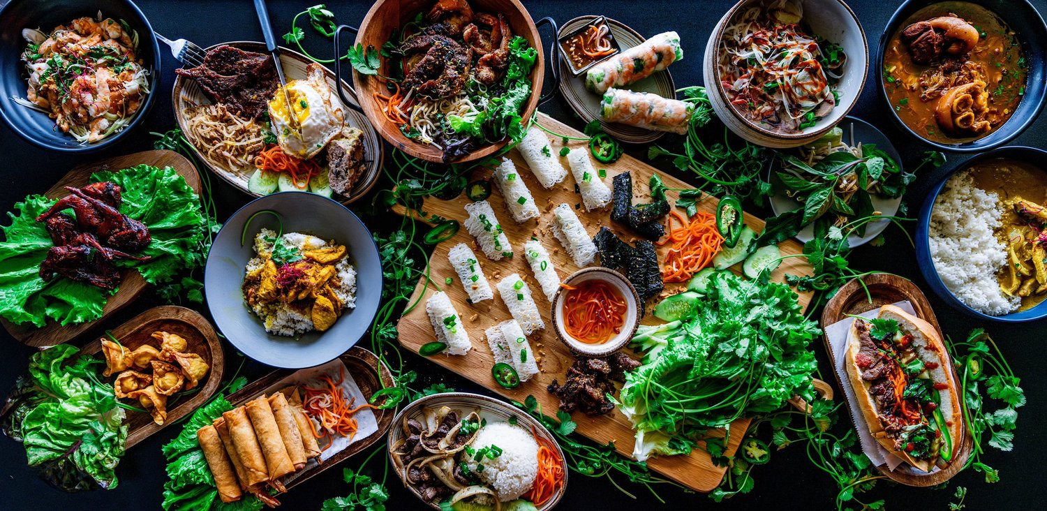 Table spread with pho, rolls, rice plates and herbs